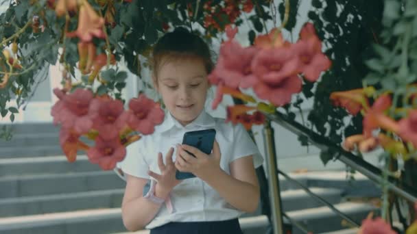 スマートフォンで遊んでいるかわいい女の子の笑顔 陽気な8 指で携帯電話を触ったり 漫画を見たり 教育アプリで楽しんだりする少女 屋外で公園にいる子供たち — ストック動画