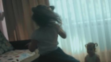Kıvırcık saçlar etrafında dönerken aktif mutlu kız evde dönüyor. Küçük kız kardeş alkışlamak için ellerini çırpıyor. Evde eğleniyorum.