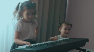 Kafkasyalı genç müzisyen kız eğlenceli aktiviteler yapıyor evde müzik eğitimi alanında piyano dersi veriyor. Küçük kız kardeş de oynamaya çalışıyor. Kızlar eğlenin.