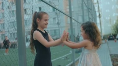 İki güzel beyaz kız bir futbol stadyumunun yakınında el çırpma oyunu oynuyorlar. Kız kardeşler yaz günü dışarıda eğleniyorlar.