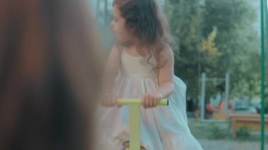 Küçük mutlu beyaz kızlar, güzel bir yaz gününde bir metalin üzerinde oturup oyun bahçesinde sallanırlar.
