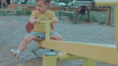 Küçük mutlu beyaz kız güzel bir yaz gününde parkta metal bir salıncakta oturuyor.