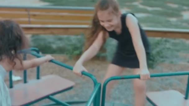 在一个阳光灿烂的夏日 两个可爱而快乐的小女孩在操场上骑着旋转木马 玩得很开心 免版税图库视频