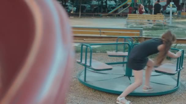 かわいい陽気な女の子が遊び場でメリーゴーラウンドに乗っていて 晴れた夏の日に楽しんでいます — ストック動画