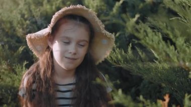 Çizgili elbiseli ve parktaki çimlerin üzerinde dinlenen güneş şapkalı güzel küçük kız. Yaz, tatil, mutlu çocukluk kavramı. Yakın çekim..