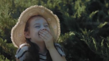 Çizgili elbiseli ve parktaki çimlerin üzerinde dinlenen güneş şapkalı güzel küçük kız. Bir şakaya gülüyorlar. Yaz, tatil, mutlu çocukluk kavramı. Yakın çekim..