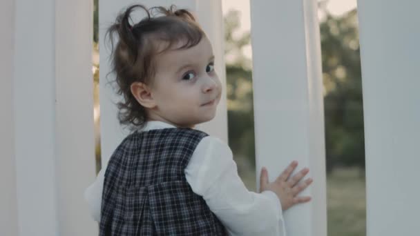 Щаслива Усміхнена Мила Дівчинка Малюк Кісками Стоїть Біля Білого Паркану — стокове відео