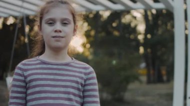 Çizgili bir elbise giymiş, parkta kameraya poz veren küçük şirin bir kızın portresi.