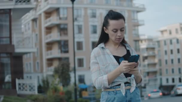住宅地に一人で立っている若い女性 携帯電話を使用して 画面を見て テキスト アプリチャットでメッセージを送信 — ストック動画