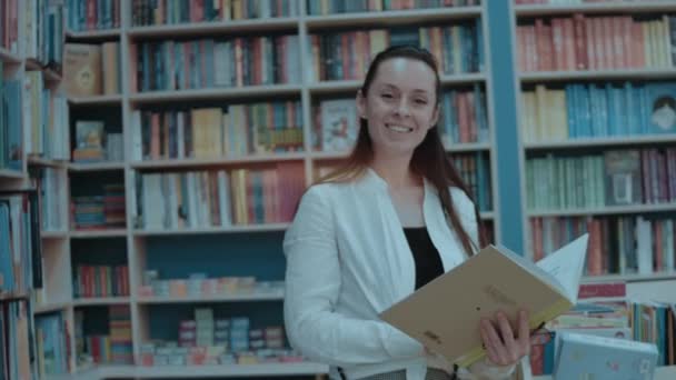 Χαμογελαστή Νεαρή Γυναίκα Περνάει Τον Ελεύθερο Χρόνο Της Στο Βιβλιοπωλείο — Αρχείο Βίντεο