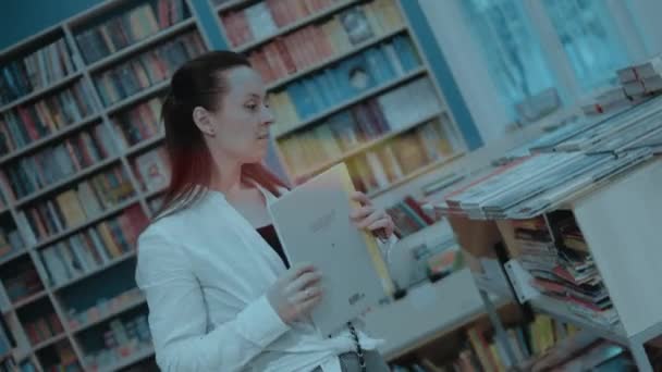 Szczęśliwa Młoda Kobieta Spędza Wolny Czas Księgarni Szukając Nowej Książki — Wideo stockowe