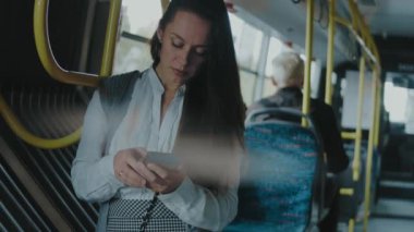 Şehir otobüsünde duran güzel genç kadın, cep telefonu ekranına bakıyor, yavaş çekim..