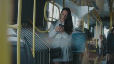 Güzel genç bir kadın şehir otobüsünde duruyor, cep telefonu ekranına bakıyor.