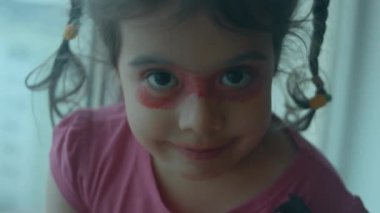 Kendine güvenen küçük beyaz kız yüzünü ruj ve göz farı ile boyamış. Küçük kız sırf eğlence olsun diye dudaklarını ve göz kapaklarını maske olarak boyadı.