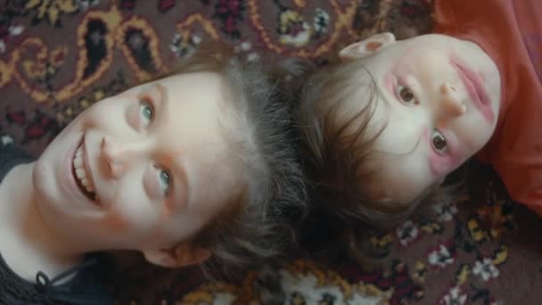 小さな白人少女が口紅と眉毛で顔を描きました 姉妹は唇とまぶたを描き 床に横たわって笑った — ストック動画