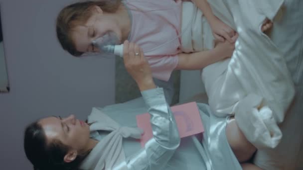 小さな女の子が病気を治療するために直面する呼吸マスクを持っている介護母親の垂直射撃 呼吸マスクによる吸入のための医療機器 スーパーママのコンセプト — ストック動画