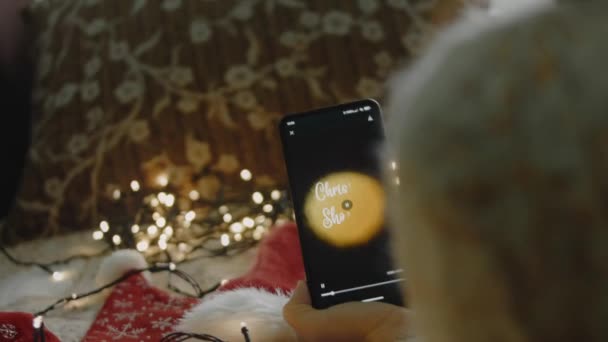 スマートフォンでクリスマスショッピングの碑文 モバイルアプリでクリスマスデザインを作るデザイナー クリスマスライトと居心地の良い雰囲気 — ストック動画