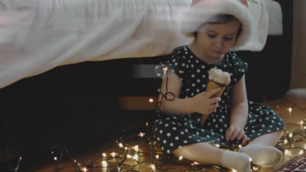 圣诞晚会上戴着圣诞老人帽的可爱小女孩在吃冰淇淋 四周都是圣诞灯 慢动作 — 图库视频影像