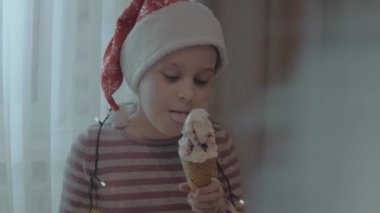 Noel Baba şapkası takan tatlı küçük kız Noel partisinde dondurma yiyor. Noel ışıkları her yerde.