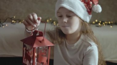 Noel Baba şapkası takan hayalperest küçük bir kız yanan mumlu bir fener tutuyor. Umut, tatil, Noel kavramı. Yavaş çekim.