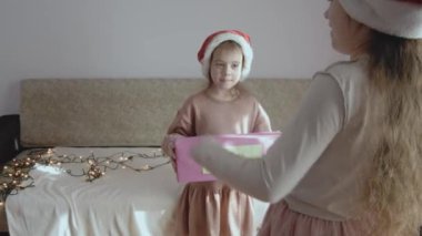 Küçük mutlu kız gizemli bir hediye kutusu tutuyor. Başka bir kız, gizemli kutunun içinde ne olduğunu tahmin eden işaretler gösteriyor. Noel arifesinde oynayan küçük kızlar