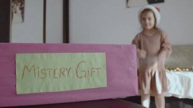 Gizemli hediye kutusu. Küçük kız, gizemli kutunun içinde ne olduğunu tahmin eden işaretler gösteriyor. Noel arifesinde çocuklar için oyun