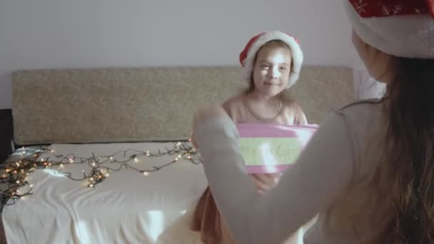 謎のギフトボックスを持っている幸せな少女 別の女の子は 謎の箱の中にあるものを推測するジェスチャーを示しています クリスマスイブで遊ぶ小さな女の子 — ストック動画