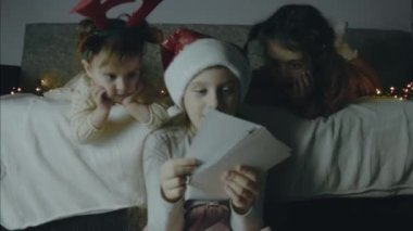 Üç küçük kız bir Noel gecesi eski resimlere bakıyorlar. Etrafta Noel ışıkları var. Noel ve bağlanma konsepti. El bilgisayarı atışı.
