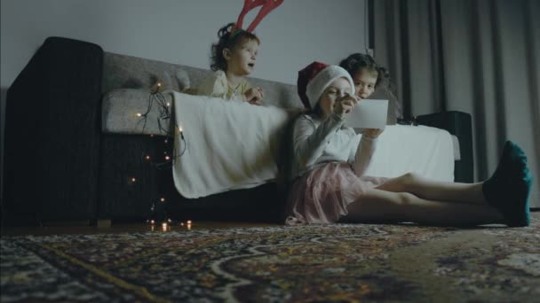 三个小女孩在一个圣诞夜晚一起看着旧照片 圣诞灯亮着圣诞节和结合的概念 慢动作 — 图库视频影像