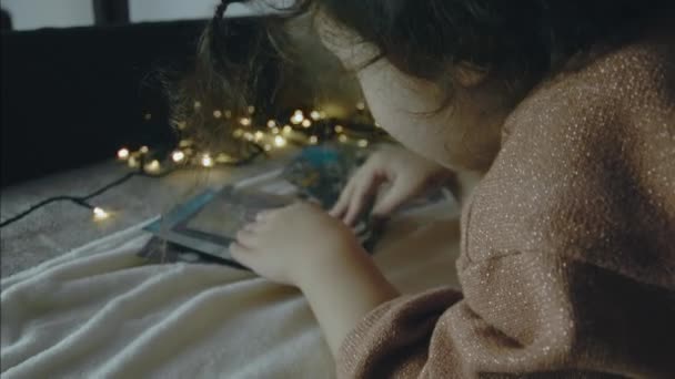 クリスマスの夜に古い写真を見る少女 周りのクリスマスライト クリスマスとレジャーのコンセプト — ストック動画
