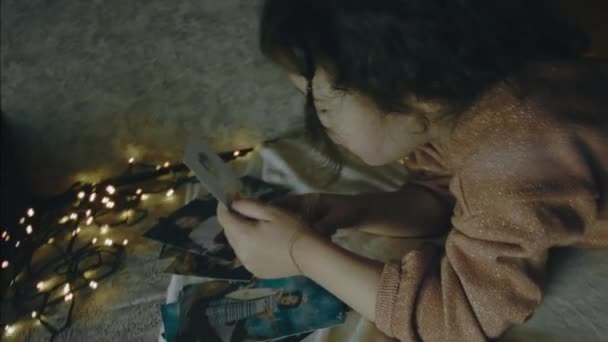Dziewczynka Ogląda Stare Zdjęcia Świąteczny Wieczór Wigilijne Światełka Koncepcja Świąt — Wideo stockowe