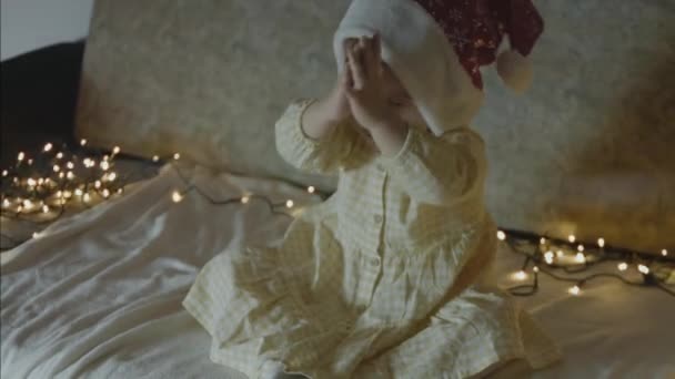 一个带着圣诞老人帽的蹒跚学步的女孩想要什么Toddler的女孩在平安夜祈祷手持射击 — 图库视频影像