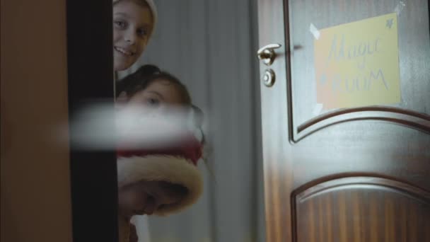 三个咯咯地笑着的小女孩从魔法室的敞开的门上看着摄像机 平安夜的享受 — 图库视频影像