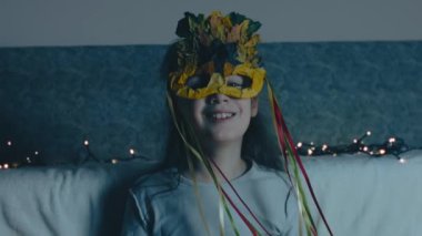 Küçük bir kızın sonbahar yaprağı maskesini çıkarıp Noel Baba şapkasını takıp kameraya gülümseyen portresi. Sonbahardan kışa geçiş. Dikey, el bilgisayarı atışı.