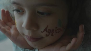 Yüzünde ayçiçeği çizimi ve tarım yazıları olan ciddi küçük bir kız. Tarım kavramı