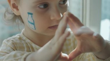 Yüzünde süt şişesi ve inek çizimleri olan sevimli küçük bir kız. Elleriyle kalp hareketlerini gösteriyor. Tarım kavramı