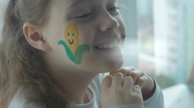 Şirin, neşeli bir kızın yüzünde mısır ve traktör çizimleri. Kalp hareketini elleriyle gösteriyor. Tarım kavramı