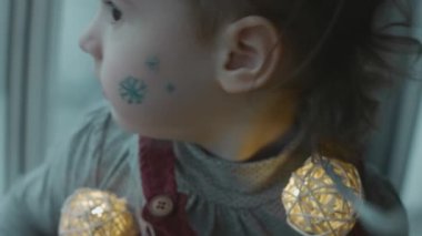 Yüzünde Noel temalı resim olan neşeli küçük kız. Yüzünde kar taneleri ve ren geyiği resmi var. Noel konsepti