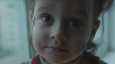 Yüzünde Noel temalı resim olan neşeli küçük kız. Yüzünde kar taneleri ve ren geyiği resmi var. Noel konsepti