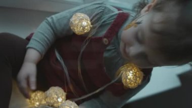 Yüzünde Noel temalı resim olan neşeli küçük kız. Noel ışıklarıyla oynamak. Noel konsepti
