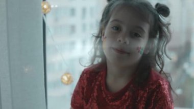 Yüzünde Noel temalı resimler olan neşeli küçük bir kız. Yüzünde hediye ve kutsal çilek resimleri var. Noel konsepti