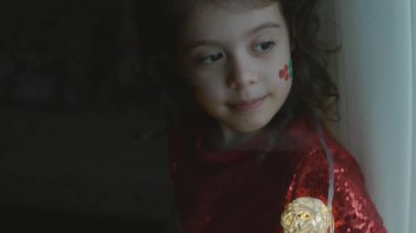 Yüzünde Noel temalı resimler olan neşeli küçük bir kız. Yüzünde hediye ve kutsal çilek resimleri var. Noel konsepti. El bilgisayarı atışı.
