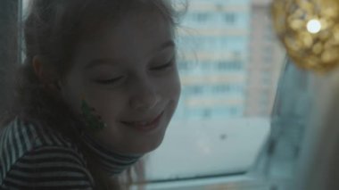 Yüzünde Noel temalı resim olan neşeli küçük bir kız. Yüzünde Noel ağacı resmi var. Noel konsepti