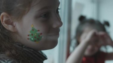 Yüzlerinde Noel temalı resimler olan neşeli küçük kızlar. Kalp işaretini elleriyle gösteriyor. Noel konsepti