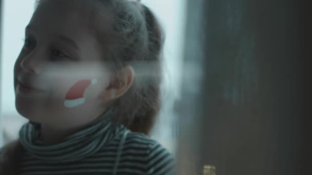 彼女の顔にクリスマスをテーマにした絵を描いた陽気な少女 サンタは顔に絵を描いている クリスマスコンセプト — ストック動画