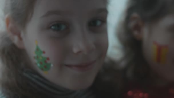 彼女の顔にクリスマスをテーマにした絵を描いた陽気な少女 顔にクリスマスツリー塗装 クリスマスコンセプト スローモーション — ストック動画