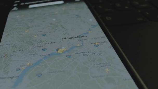 スマートフォン画面のグローバルマップ上のオンラインフライト追跡 フィラデルフィア アメリカ 船積み 物流コンセプト — ストック動画