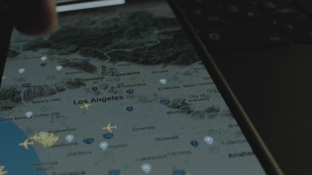 スマートフォン画面のグローバルマップ上のオンラインフライト追跡 ロサンゼルス アメリカ 船積み 物流コンセプト — ストック動画