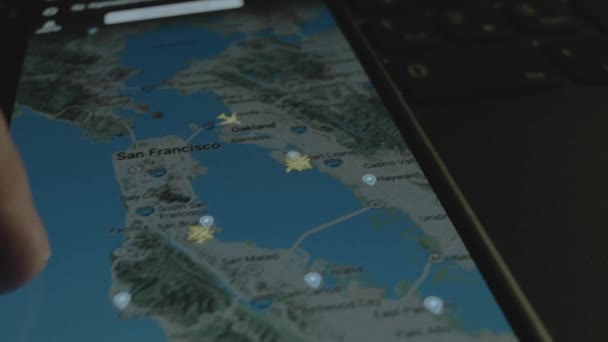 スマートフォン画面のグローバルマップ上のオンラインフライト追跡 サンフランシスコ アメリカ 船積み 物流コンセプト — ストック動画