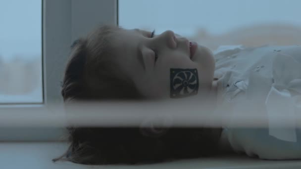 彼女の顔にコンピュータファン絵を描いた陽気な少女 閉じた目で窓に横たわっている コンピューターコンセプト スローモーション — ストック動画
